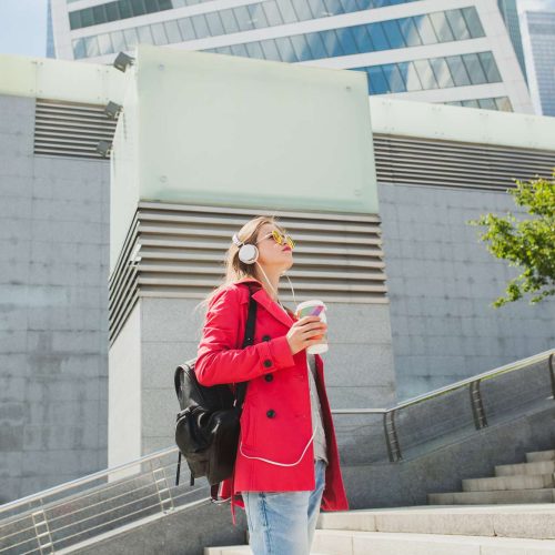 img_mcgrath_foto_canada_2000_young-hipster-woman-pink-coat-jeans-street-with-backpack-coffee-listening-music-headphones-wearing-sunglasses